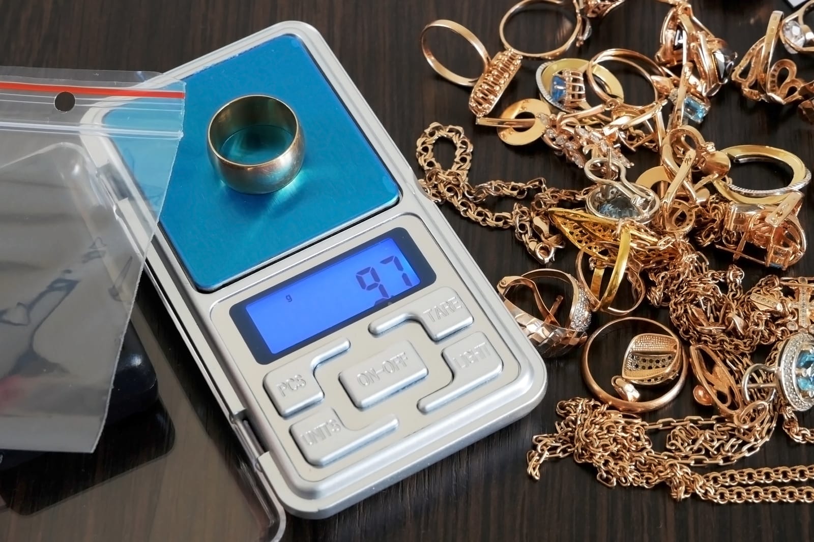 Anillo de oro sobre una báscula digital de bolsillo junto a un montón de cadenas, anillos y pendientes de oro